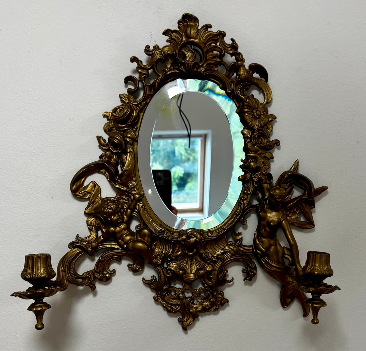 Gazdagon díszített, rokokó ihletésű fali tükör kétoldali gyertyatartó karokkal.